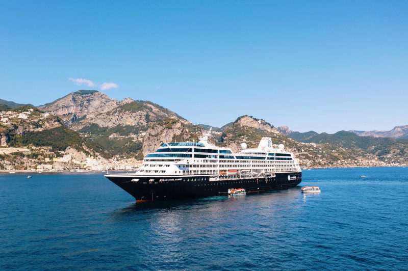 Azamara Journey cruise ship gliding across calm blue waters with a backdrop of tropical islands.